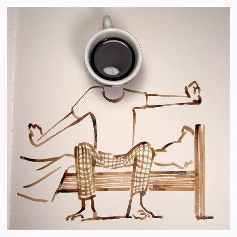 a cup of coffee sitting on top of a table next to a drawing of a man laying on a bench