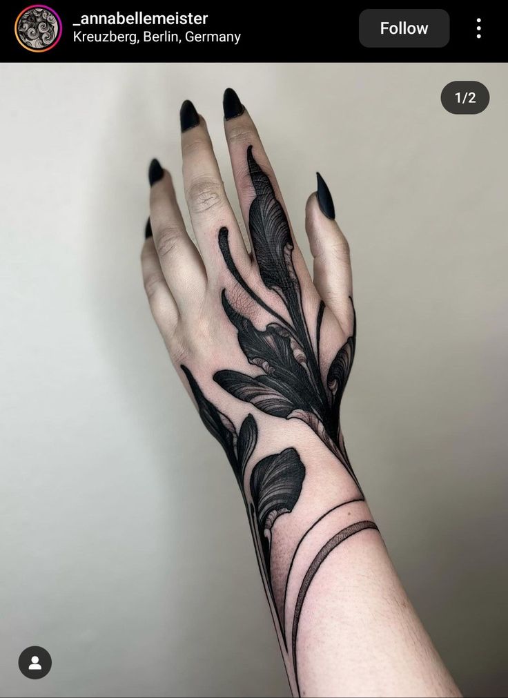 a woman's hand with black ink on it and an intricate feather tattoo design