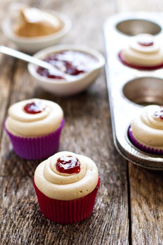 cupcakes with white frosting and jam on them sitting next to a muffin tin