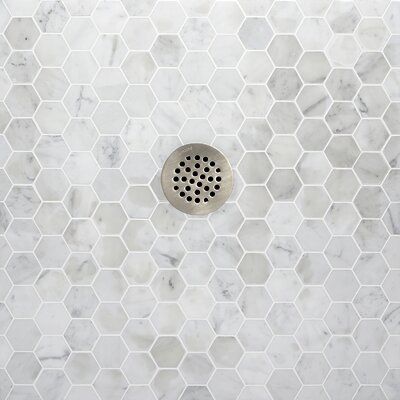 a white marble tiled shower wall with hexagonal holes in the middle and a metal grate on the side