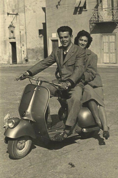 a man and woman riding on the back of a scooter in an old photo