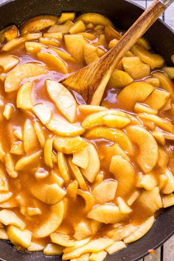 apples are being cooked in a skillet with a wooden spoon and some brown sauce