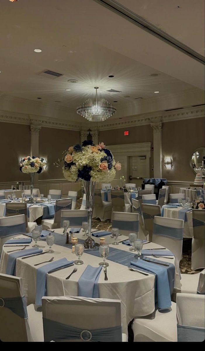 a banquet room set up with blue and white table cloths, centerpieces and flowers