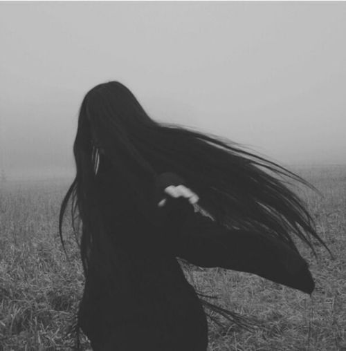 a black and white photo of a woman with long hair in the middle of a field