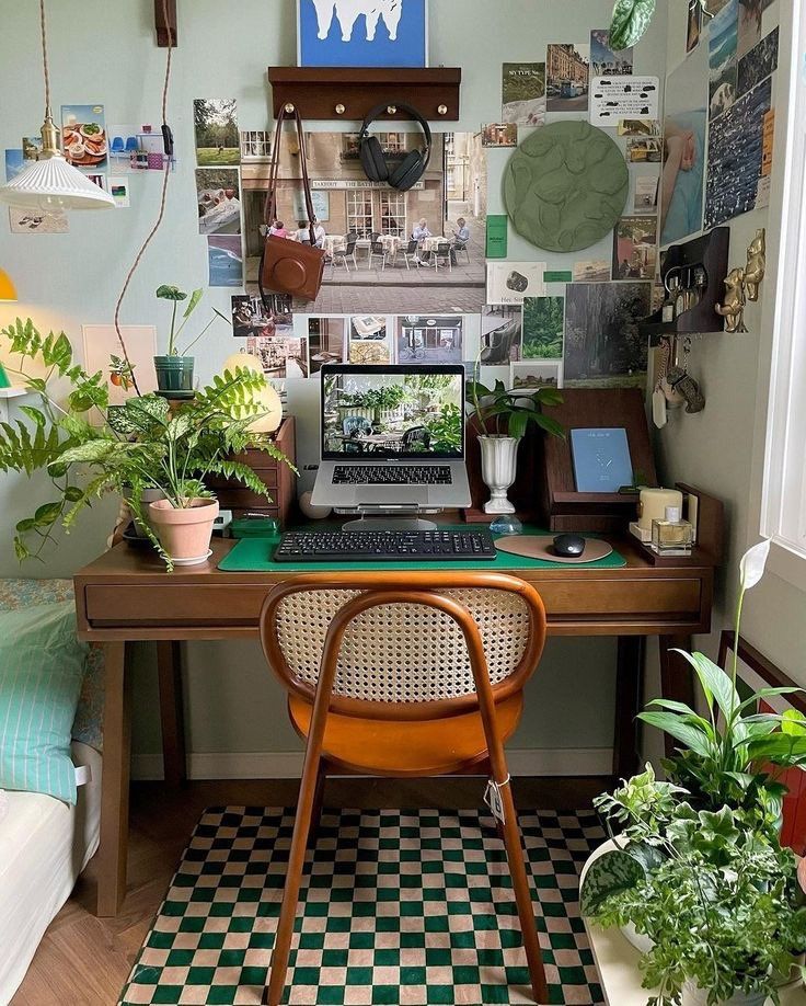 a laptop computer sitting on top of a wooden desk next to a green chair and potted plants