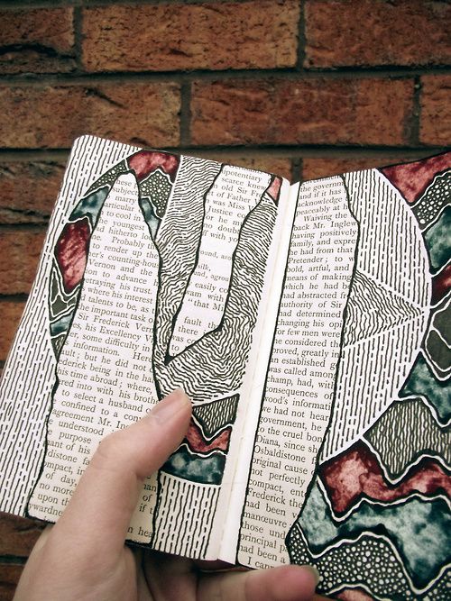 a person holding an open book in front of a brick wall with designs on it