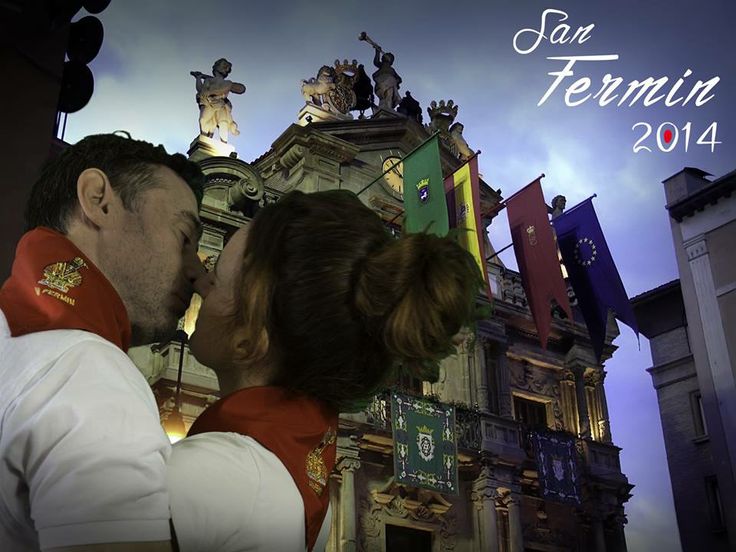 a man and woman kissing in front of a building with flags on the top of it