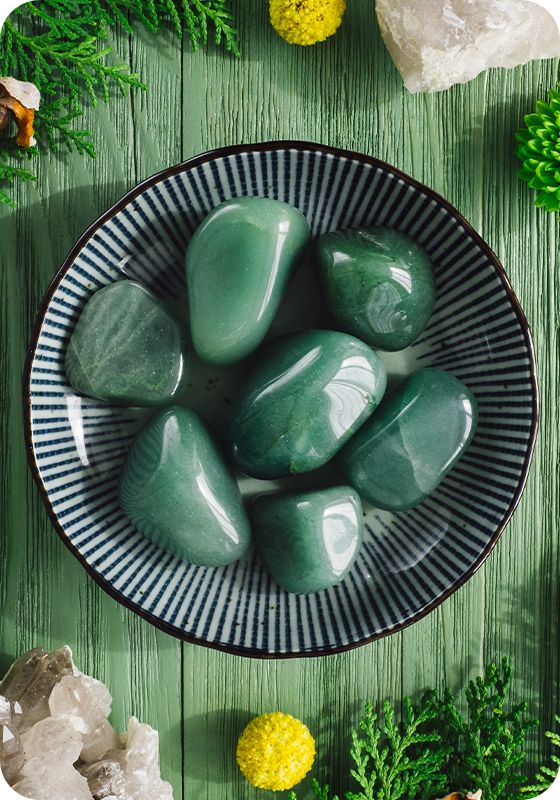 green rocks in a bowl surrounded by pine branches and other decorations on a wooden table