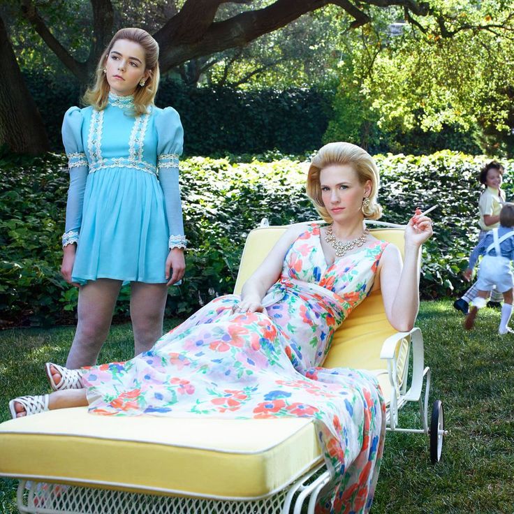 two women in dresses are sitting on lawn chairs and one woman is standing next to her