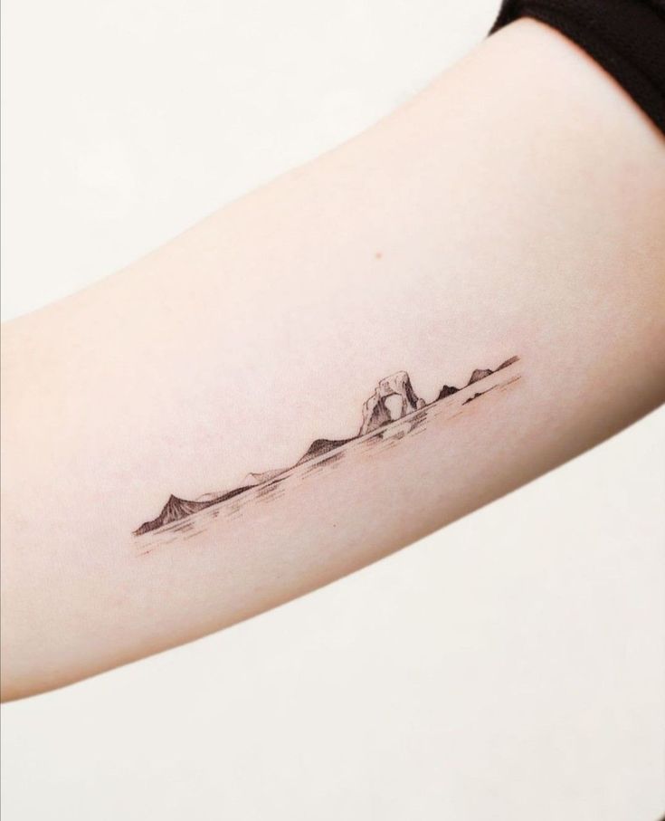 a woman's arm with a small mountain tattoo on the left side of her arm