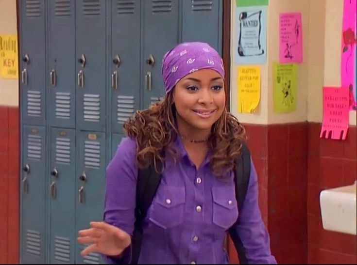 a woman with a purple shirt and head scarf standing in front of lockers holding her hands out