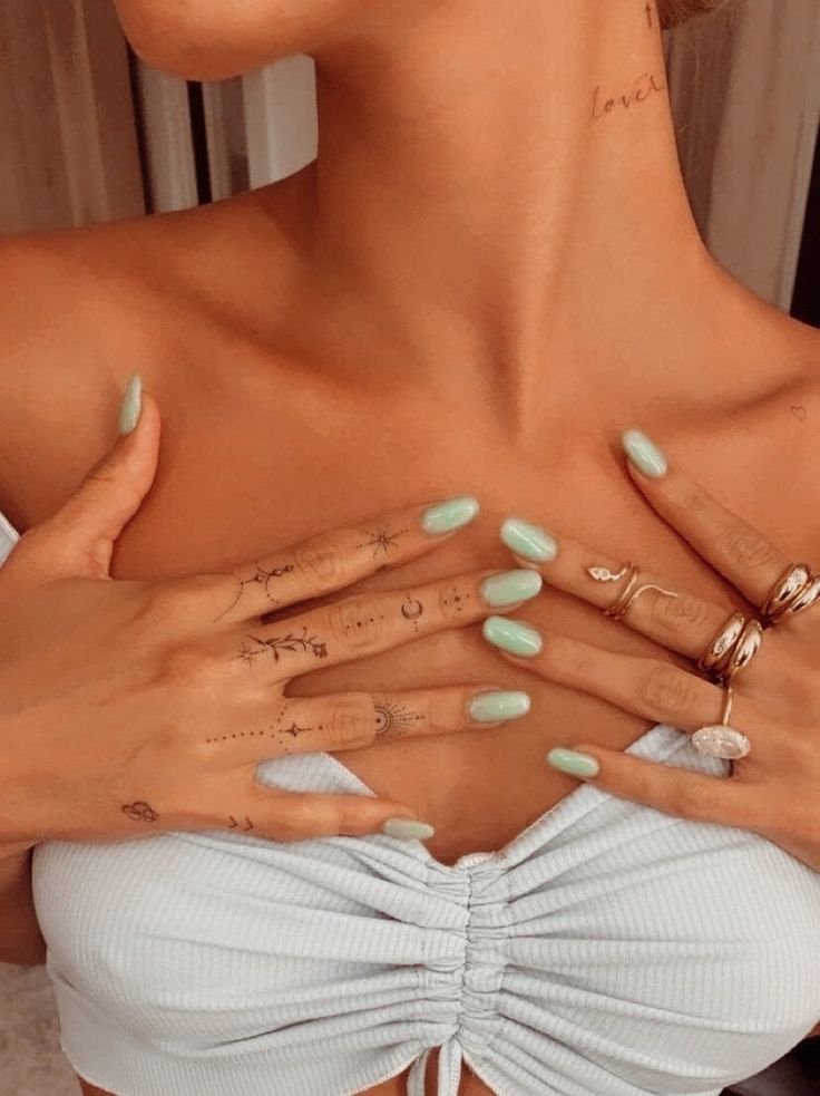 a woman with green nail polish holding her hands on her chest and showing off her tattoos