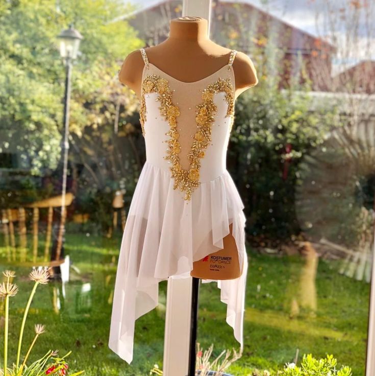 a white dress with gold sequins is on display in front of a garden