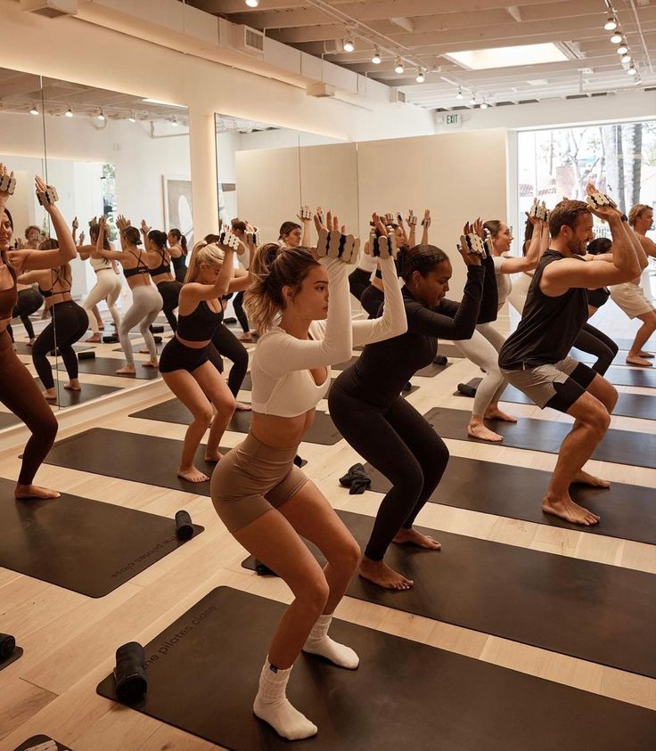 a group of people doing yoga poses in a large room with mirrors on the wall