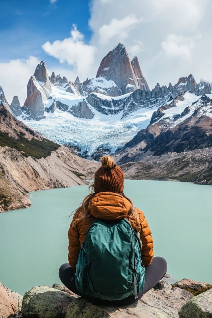 a person sitting on top of a rock next to a body of water with mountains in the background