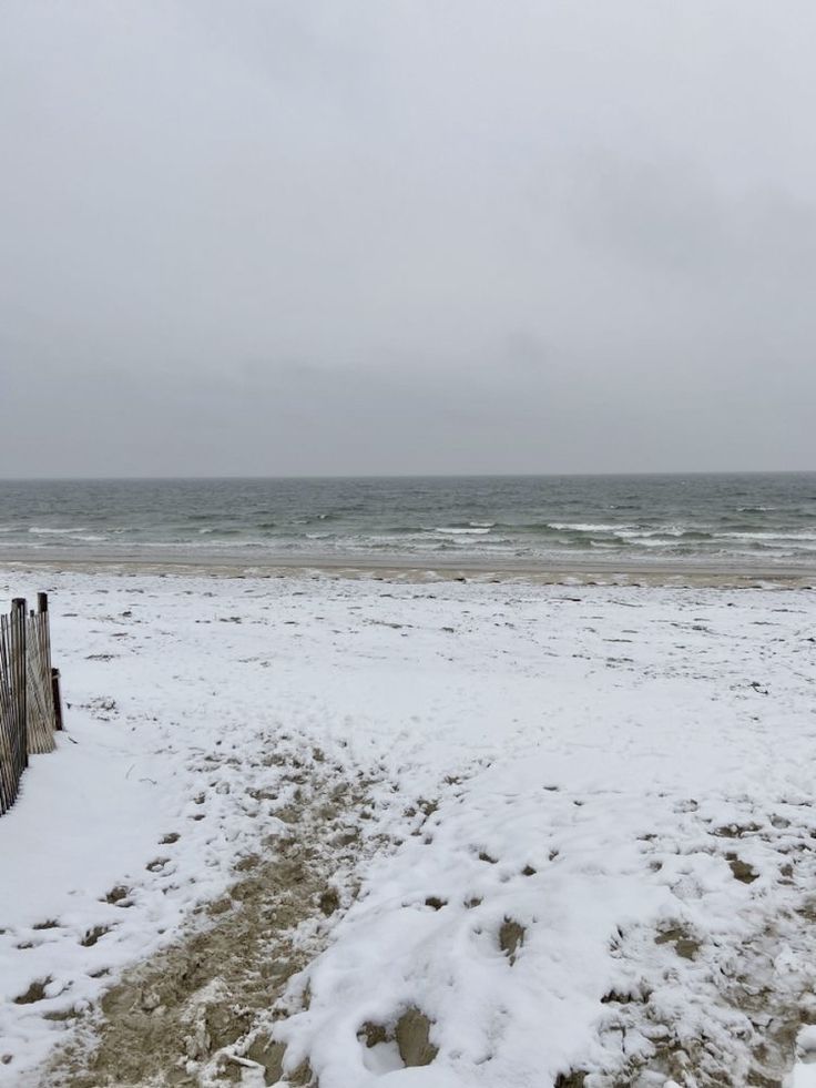 a beach covered in snow next to the ocean on a cloudy day with no people