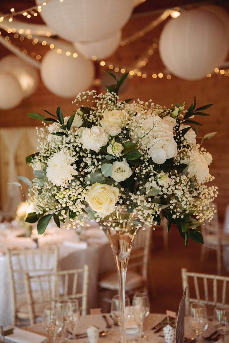 a vase filled with white flowers sitting on top of a table next to other tables