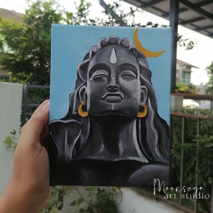 a person holding up a small painting of a buddha head with the moon above it