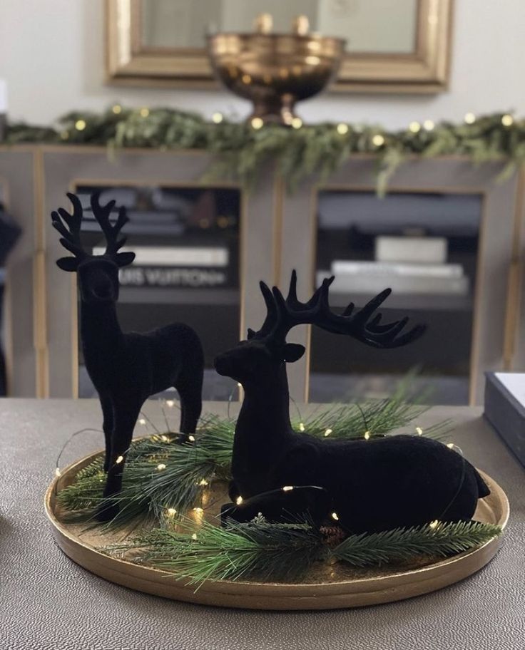 two black deer figurines sitting on top of a wooden tray next to a christmas tree