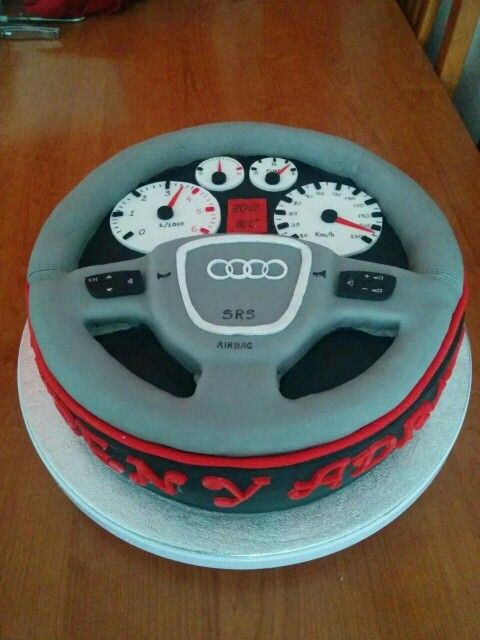 an audi car steering wheel cake with red and white piping on the front, sitting on a wooden table