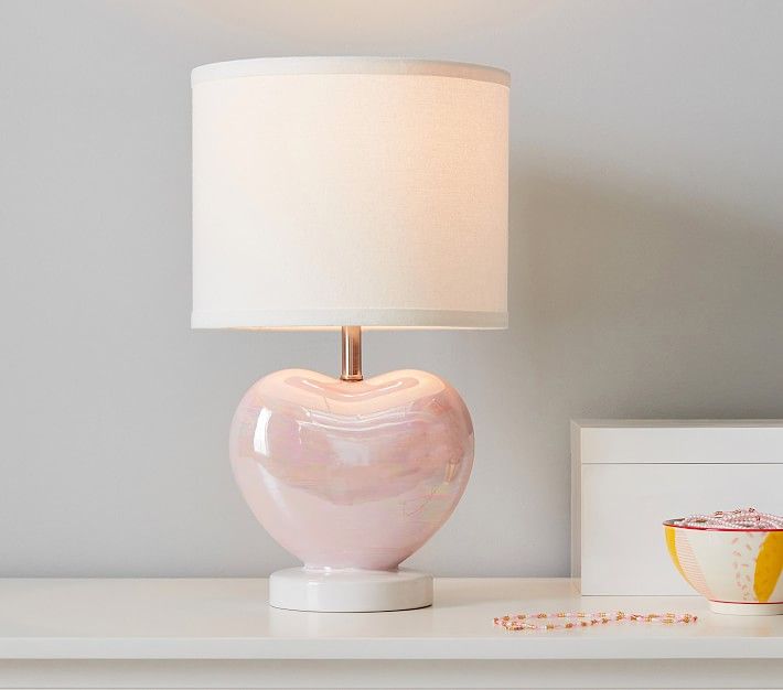 a pink heart shaped lamp sitting on top of a white table next to a bowl