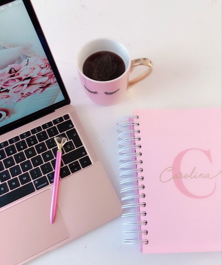 a laptop computer sitting on top of a desk next to a pink notebook and cup of coffee