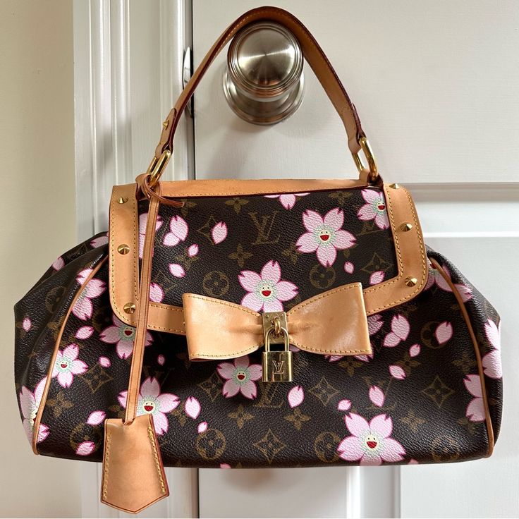 This Ultra-Rare Louis Vuitton Cherry Blossom Sac Retro Bag Is A Coveted Piece From The Exclusive 2003 Collection, Designed By The Iconic Duo Takashi Murakami And Marc Jacobs. Celebrated For Its Timeless Elegance And Feminine Charm, This Collectible Bag Perfectly Captures Vintage Flair With Its Exquisite Hardware, Including Beautiful Studs, A Signature Padlock, And An Eye-Catching Bow Detail. Product Details: Style: Louis Vuitton Top Handle Bag Collection: 2003, Designed By Marc Jacobs Material: Brown Coated Canvas With Floral Monogram Cherry Blossom Print Hardware: Brass Trim: Leather Interior: Alcantara Lining With Single Interior Pocket Features: Flat Handle With A 4 Louis Vuitton Cherry Blossom White, Louis Vuitton Cherry Blossom, Louis Vuitton Murakami Bag Flower, Louis Vuitton Cherry Blossom Bag, Louis Vuitton Top, Pink And Brown Louis Vuitton Bag, Louis Vuitton Limited Edition, Cherry Blossom Print, Retro Bags