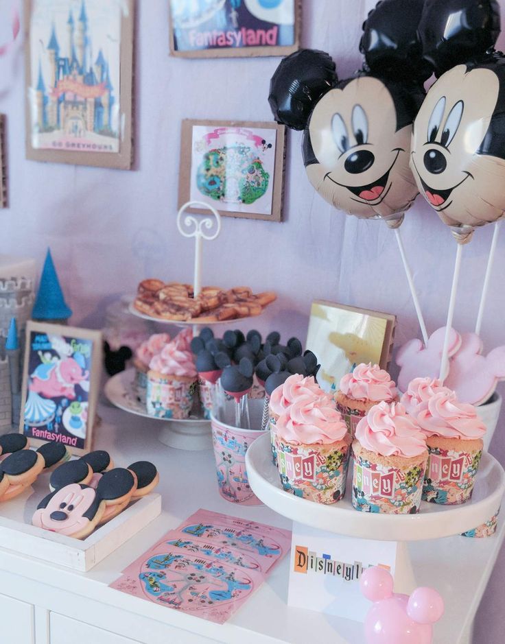 a table topped with cupcakes and mickey mouse balloons