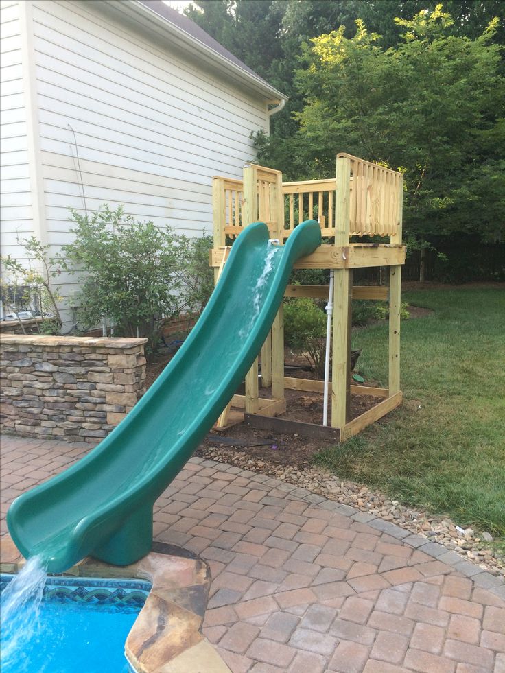 a slide in the back yard next to a swimming pool with a wooden deck and stairs