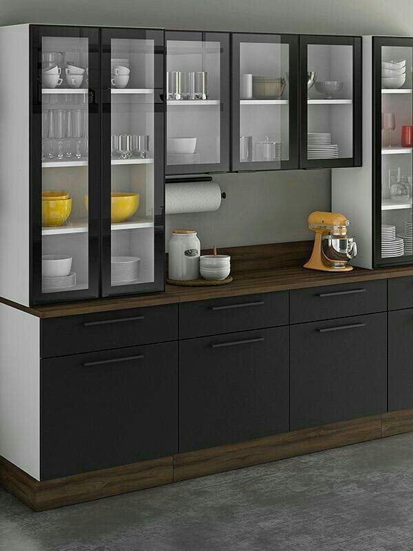 an empty kitchen with black cabinets and white dishes on the counter top, in front of a gray wall