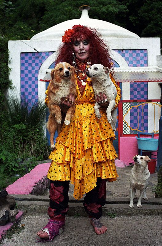 a woman with red hair holding two dogs and standing in front of a white structure