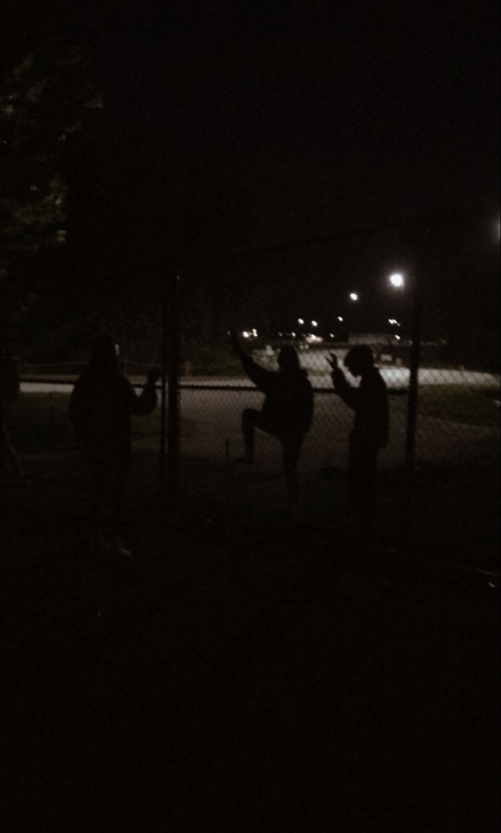 some people are playing frisbee at night in the dark by a chain link fence