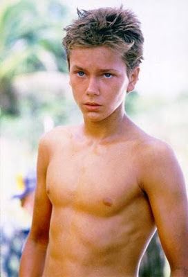 a shirtless young man with no shirt standing in front of some trees and bushes