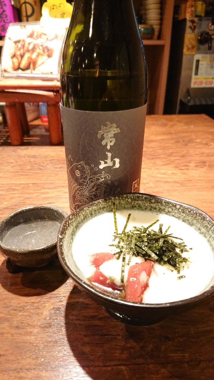 a bottle of wine sitting next to a bowl of food and a plate on a table