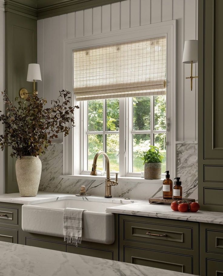 a white kitchen sink sitting under a window next to a vase with flowers in it