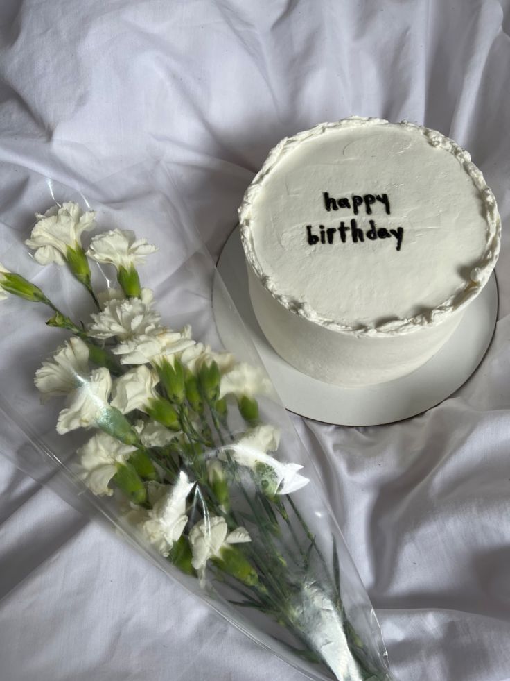 a birthday cake and some flowers on a white sheet