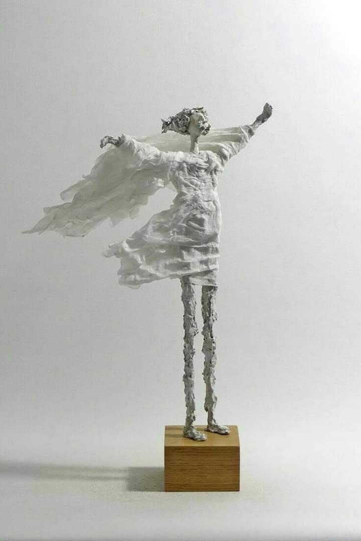 a sculpture of a woman with her arms outstretched on a wooden block in front of a white background