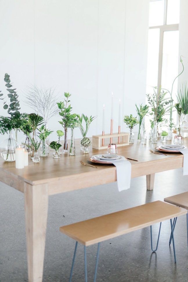 a wooden table with two benches next to it and plants in vases on top