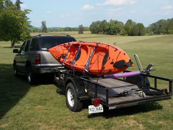 an orange kayak sitting on the back of a trailer in a field next to a car