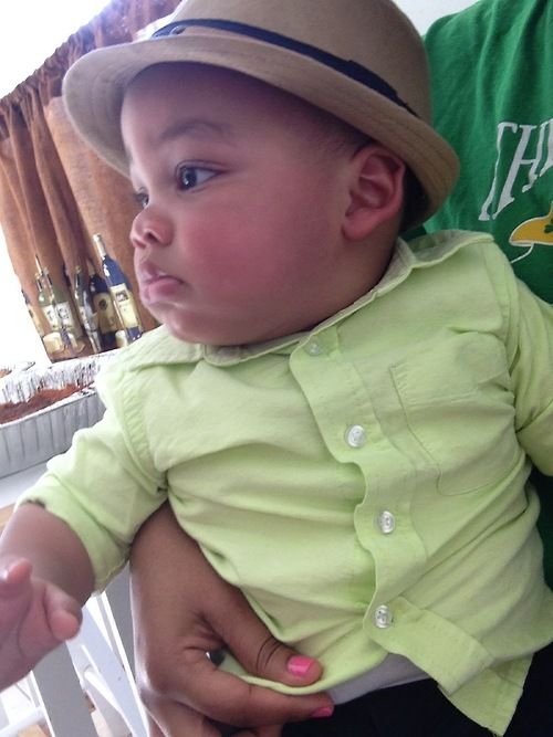 a man holding a baby wearing a green shirt and hat with his hands on the hips