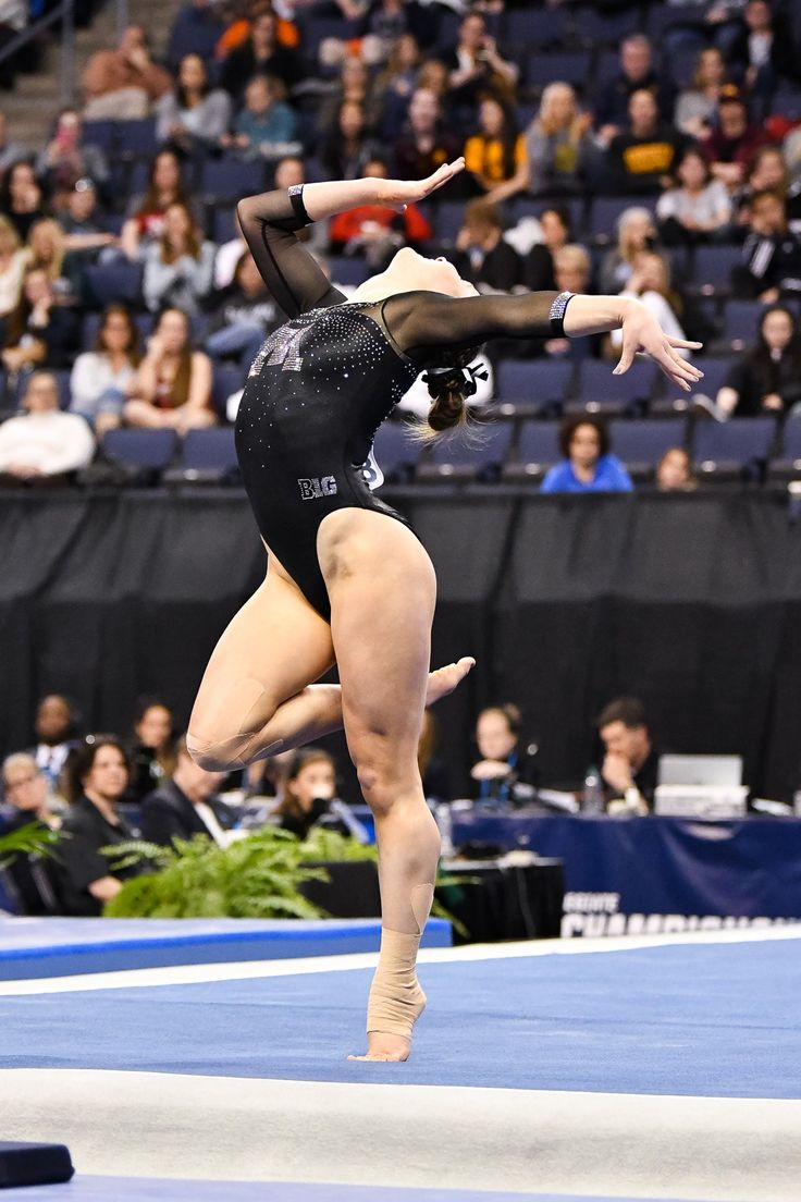 a woman is doing a trick on the balance beam in front of an audience at a competition