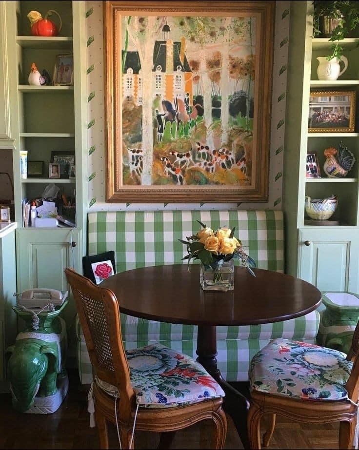 two chairs and a table in front of a painting on the wall with shelves behind it