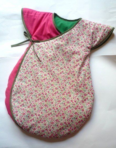 a baby sleeping bag laying on top of a white sheet covered in pink and green fabric