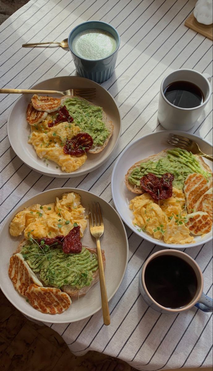 three plates with food on them sitting on a table next to two cups of coffee