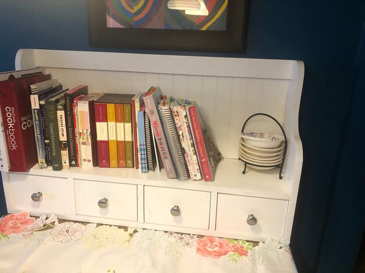 a bookshelf filled with lots of books on top of a white dresser next to a painting