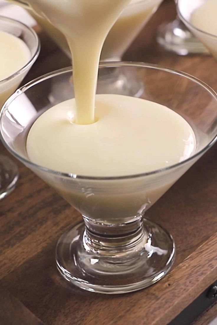 a person pouring milk into small glasses on a wooden table with other dishes in the background