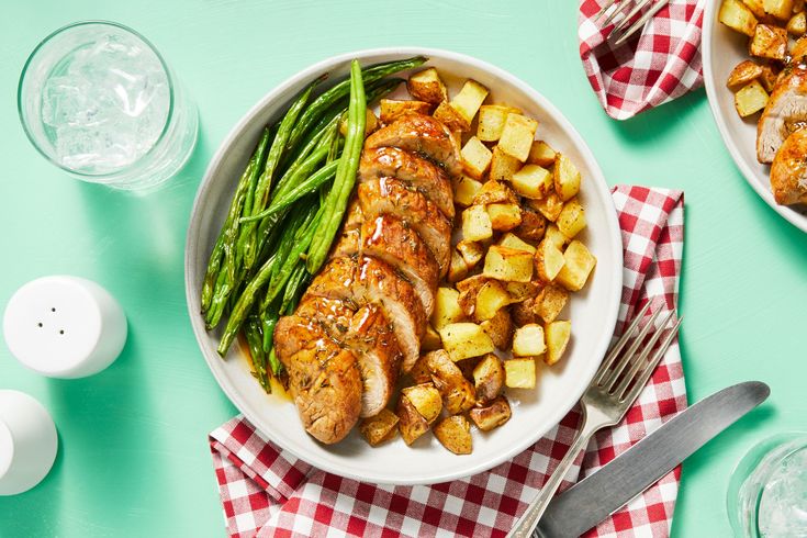 two plates filled with chicken, potatoes and green beans on top of a checkered table cloth