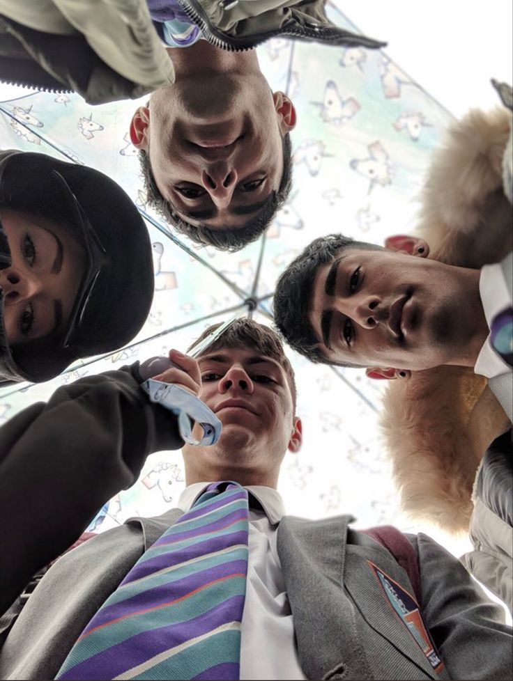 four men are standing in a circle holding an umbrella and talking on their cell phones