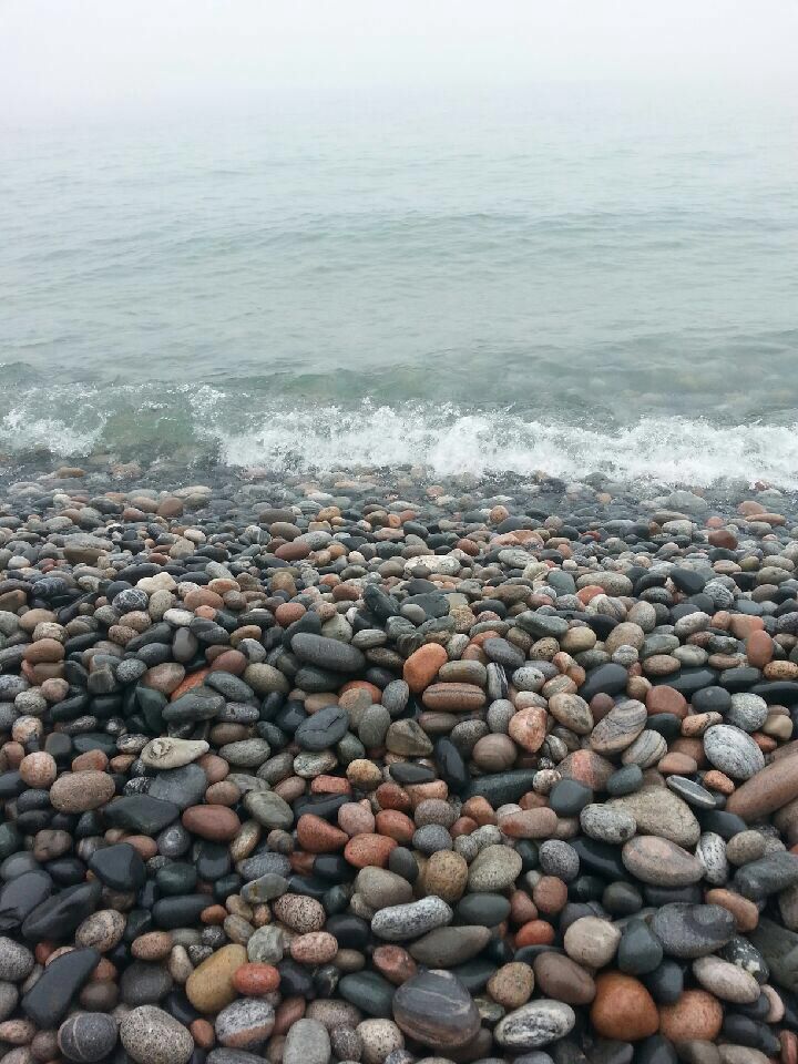 the beach is covered with rocks and pebbles as waves roll in on the ocean shore