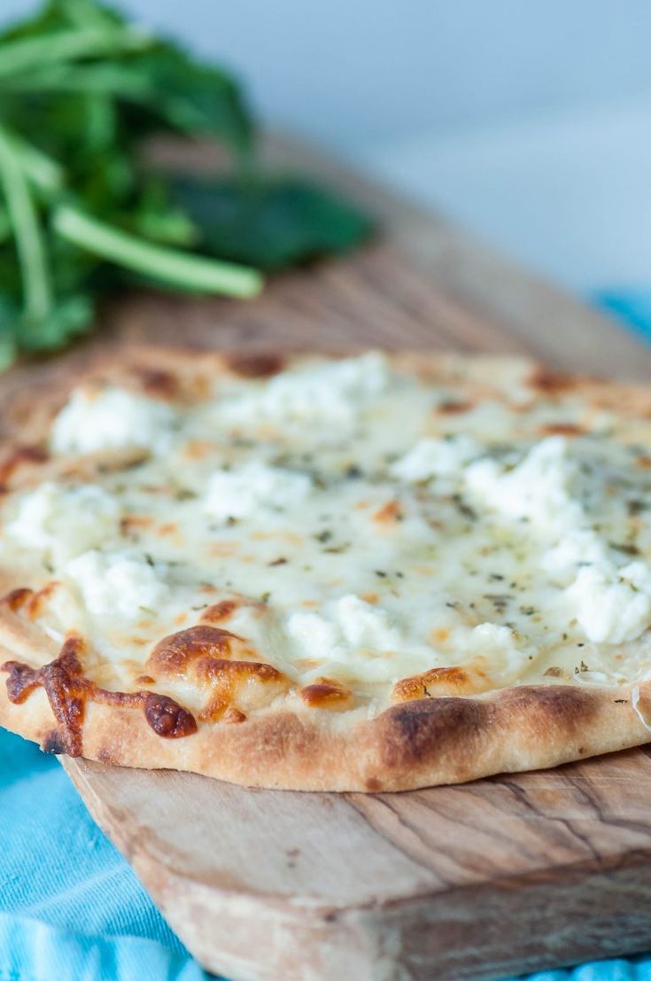 a close up of a pizza on a cutting board with cheese and spinach in the background